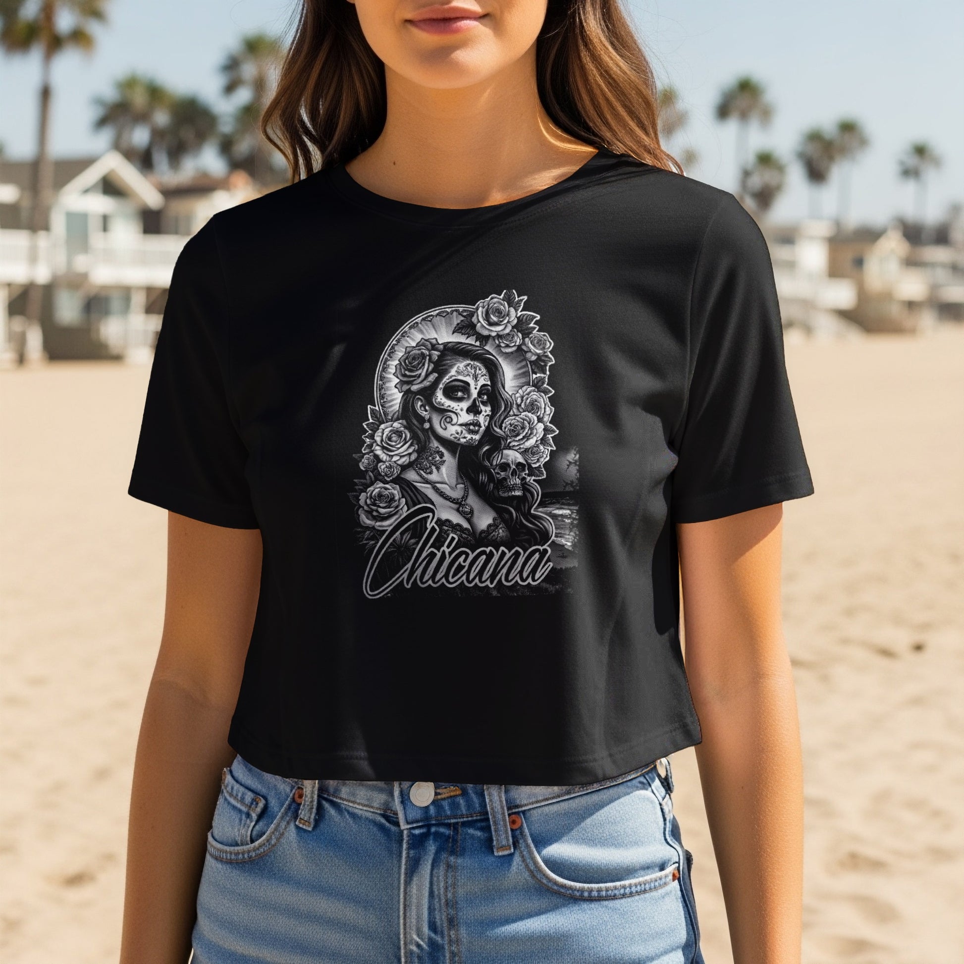 Black crop t-shirt with Chicana skull and rose graphic on a beach.