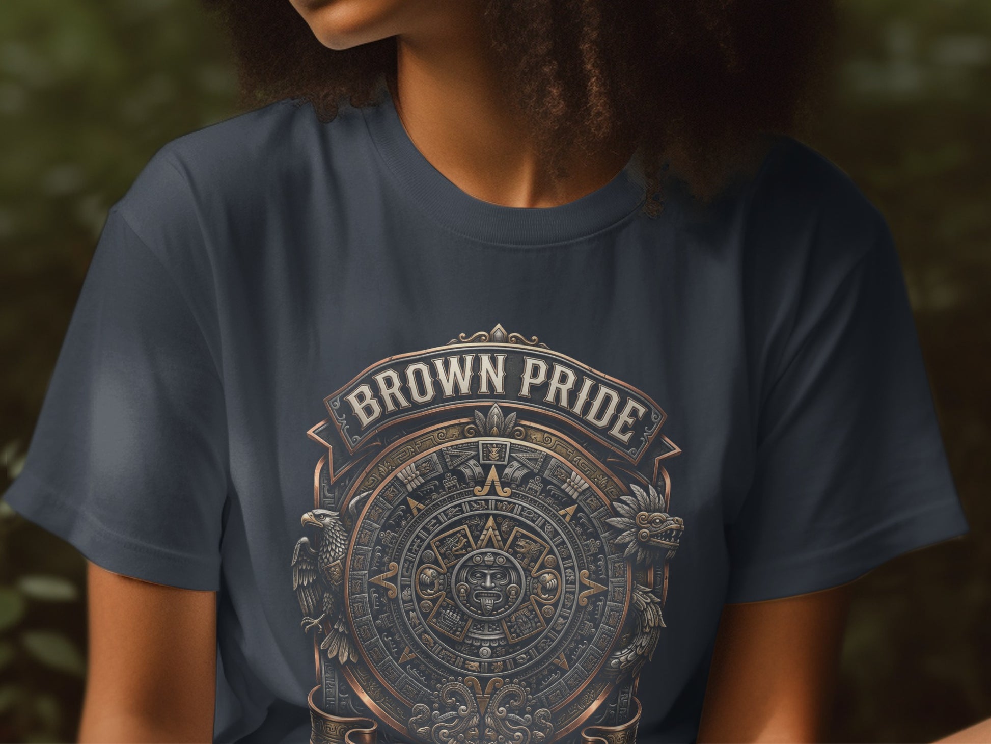 Dark t-shirt with circular Aztec-inspired "Brown Pride" graphic and flanking mythical creatures.