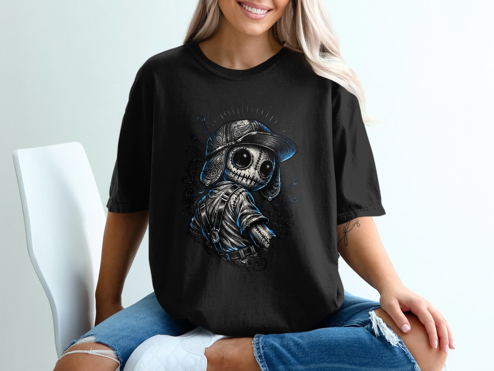 Black t-shirt with a stitched doll wearing a cap and backpack, front view.