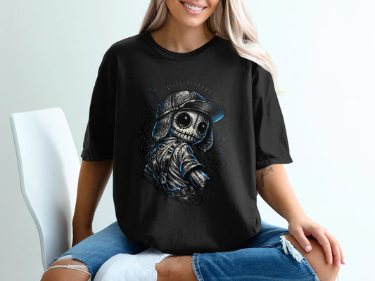 Black t-shirt with a stitched doll wearing a cap and backpack, front view.