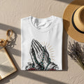 White t-shirt with praying hands, rosary, roses, and sunburst graphic.