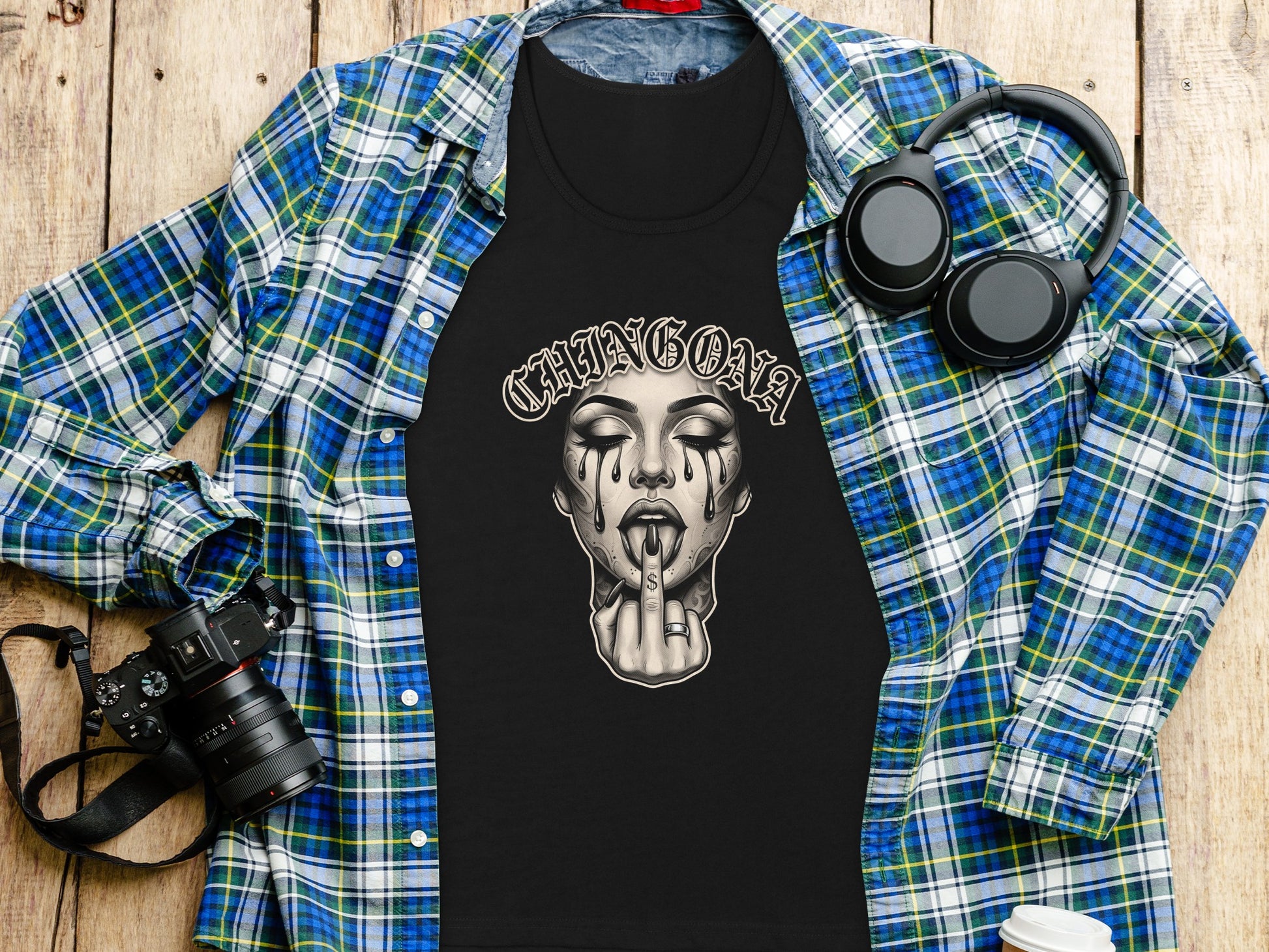 Black t-shirt with "CHINGONA" text and crying woman graphic, laid flat with camera and headphones.