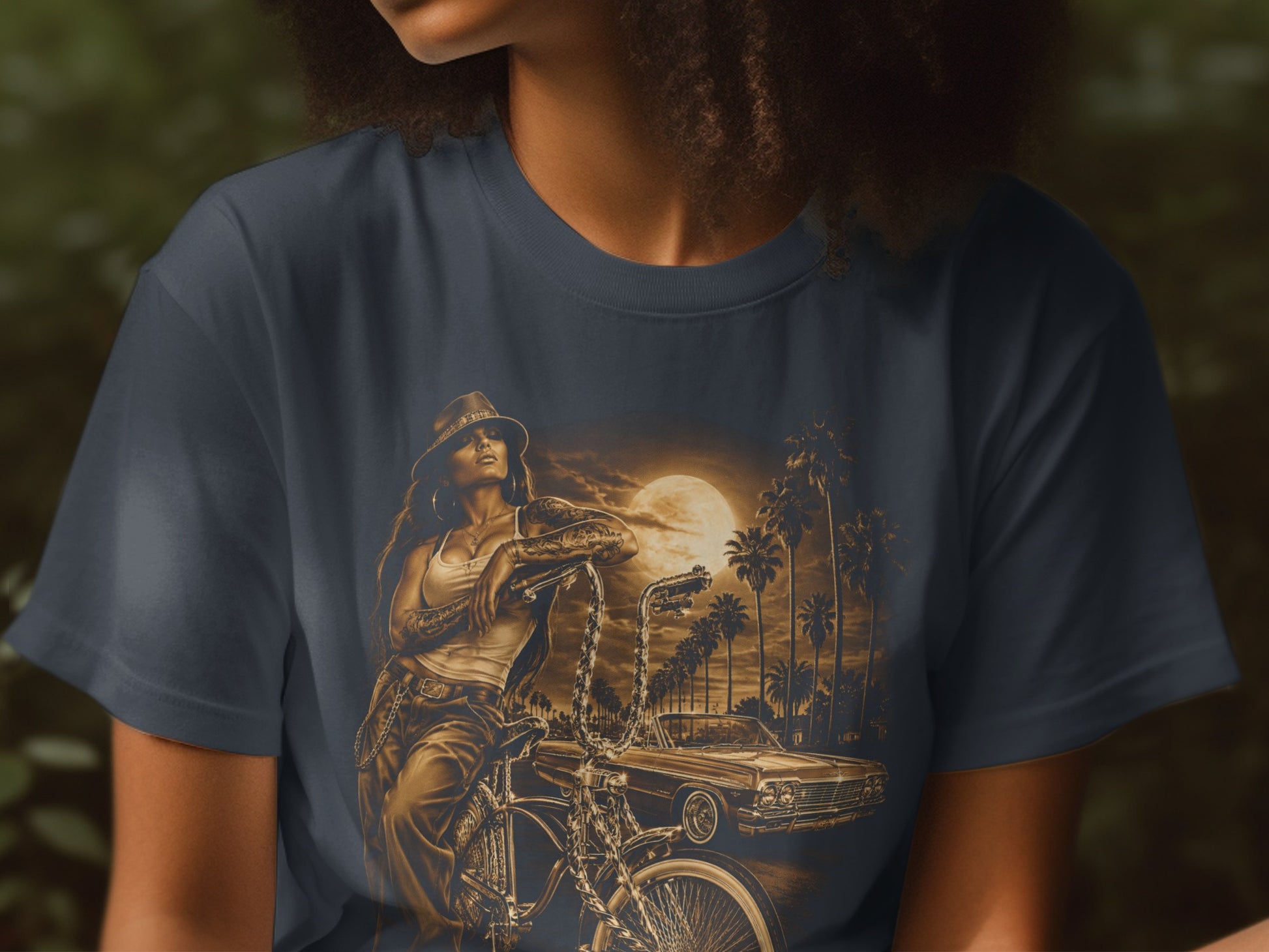 T-shirt graphic of a woman and a lowrider car against a sunset with palm trees.