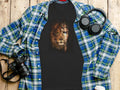 Black t-shirt with lion's face, half human, half divine, on wooden background.