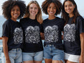 Four smiling women wearing black t-shirts with a detailed graphic design.