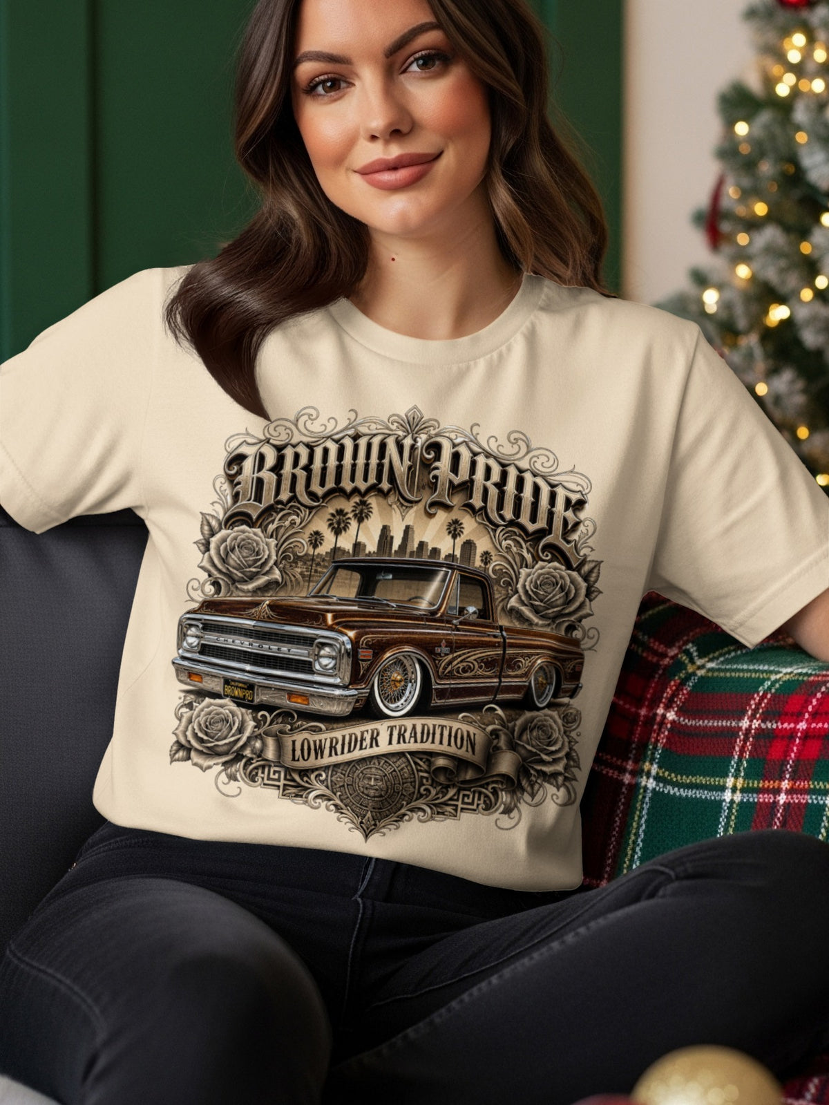 Cream t-shirt with "BROWN PRIDE LOWRIDER TRADITION" text, a vintage brown pickup truck, roses, and cityscape.