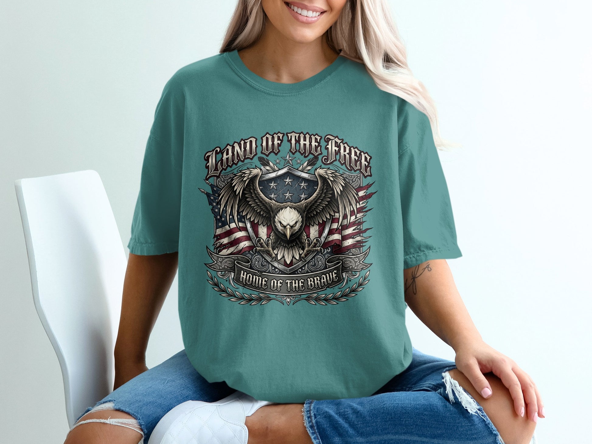 "Land of the Free, Home of the Brave" text with eagle and flag graphic on teal t-shirt.