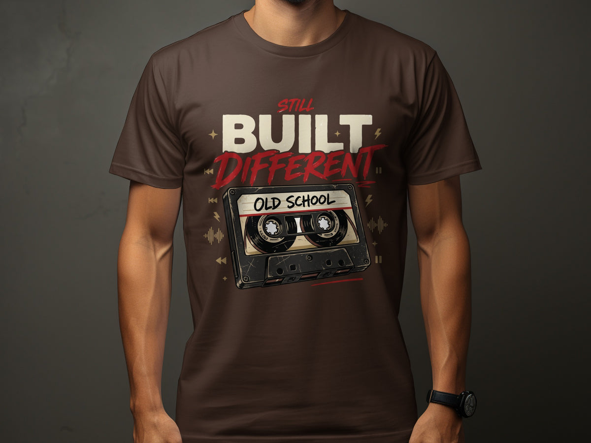 Brown t-shirt with text "STILL BUILT DIFFERENT" and an old school cassette tape.