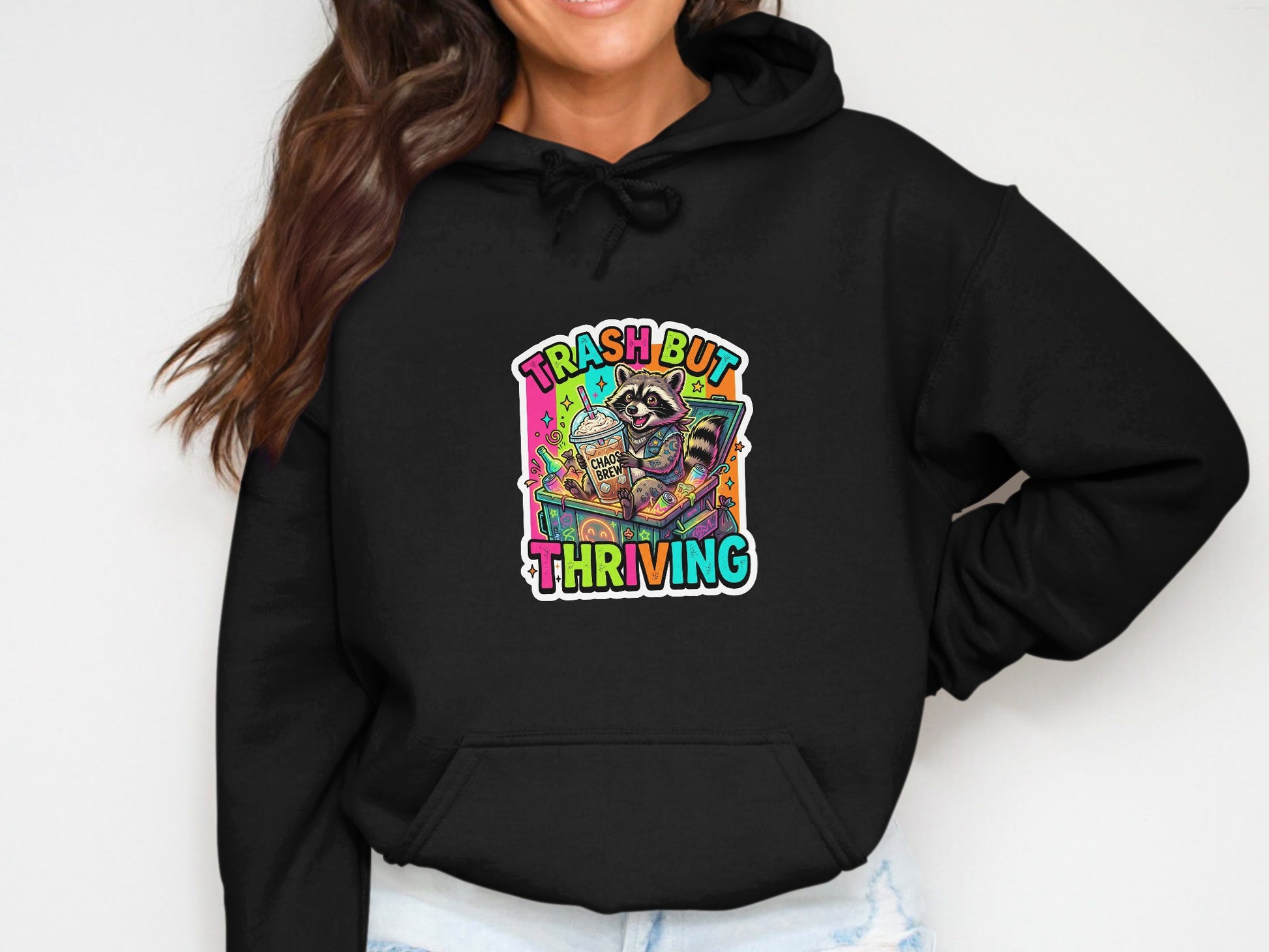 Black hoodie with a raccoon in a box, holding a coffee cup and text "Trash but Thriving".