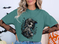 Teal t-shirt with a stitched doll illustration wearing a baseball cap and overalls.
