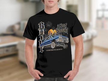 Black t-shirt with blue lowrider car, palm trees, city skyline, and text.