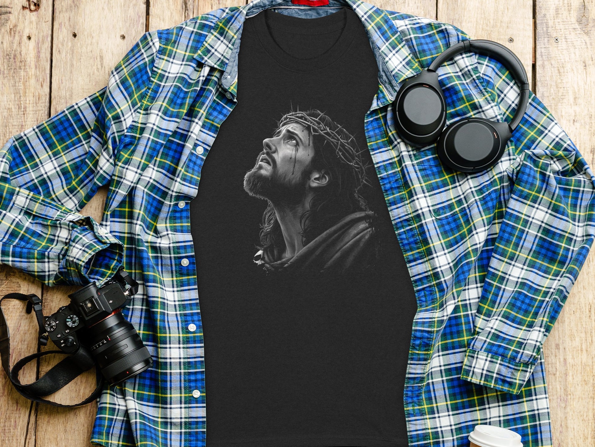 T-shirt with Jesus Christ graphic, headphones, and camera on a wooden surface.