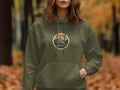Olive green hoodie with circular graphic of mountains, trees, and van with text.