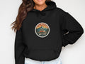 Black hoodie with a circular patch featuring a camper van and mountains, text 