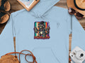 Light blue hoodie with cartoon raccoon holding paint cans, 