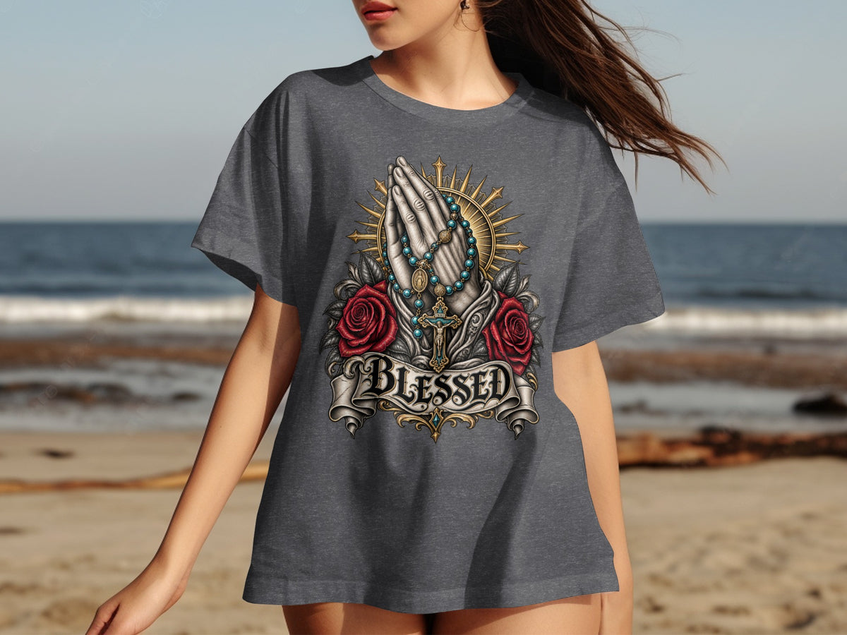 Praying hands with rosary, roses, cross, and "Blessed" text on a t-shirt.