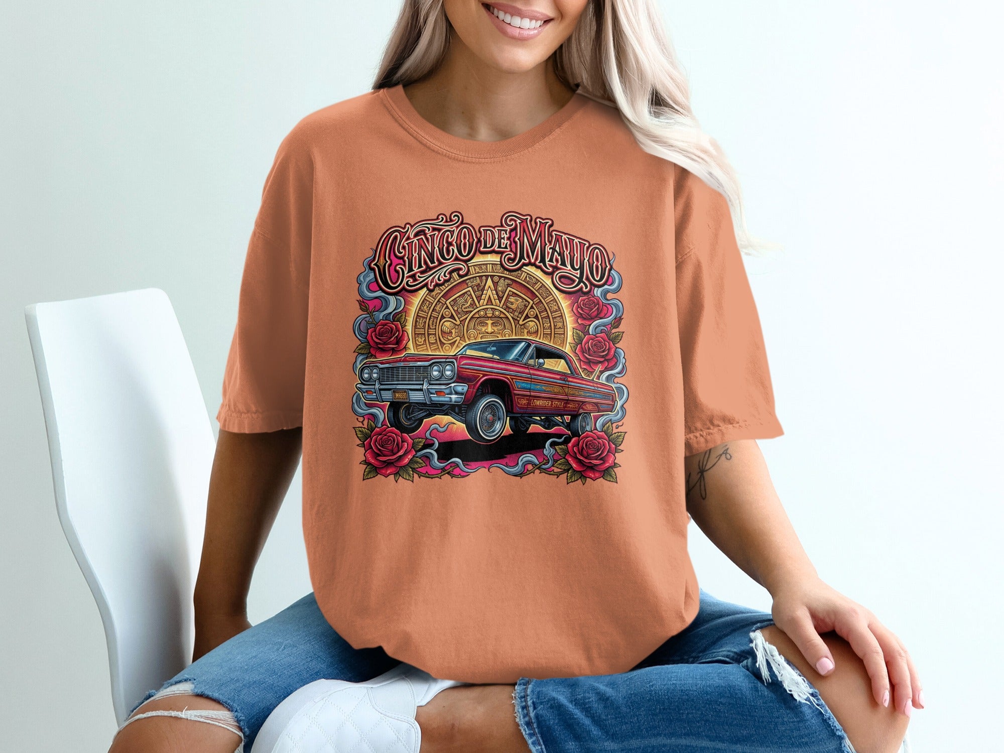 Cinco de Mayo t-shirt featuring a classic red lowrider car surrounded by roses and Aztec sun stone design.