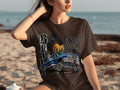 Brown t-shirt with graphic of a blue classic car, palm trees, sunset, and text.