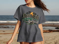 Dark gray t-shirt with graphic of green lowrider, palm trees, and sunset. Text says 