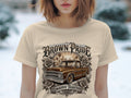T-shirt graphic with a brown lowrider truck, roses, city skyline, and text.