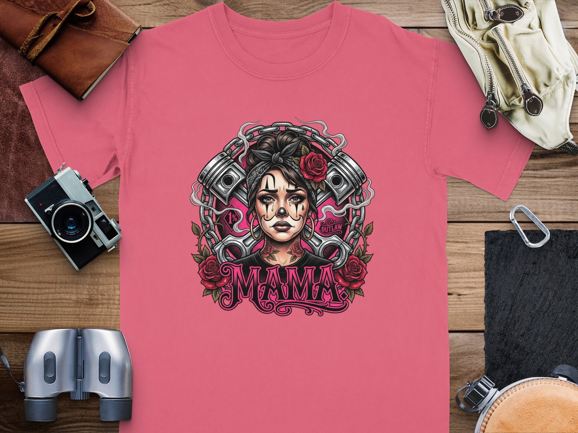 Woman with tattoos and roses in hair, "Mama Outlaw" text on pink t-shirt.
