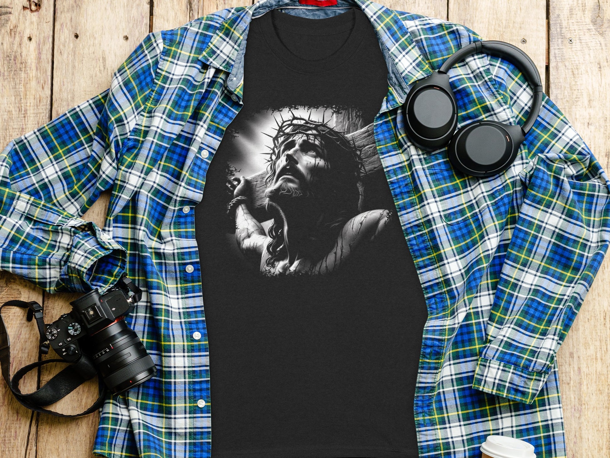 Black t-shirt with Jesus Christ on the cross graphic, laid flat with headphones and camera.