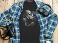 Black t-shirt with skull couple graphic, laid on a plaid shirt with headphones.