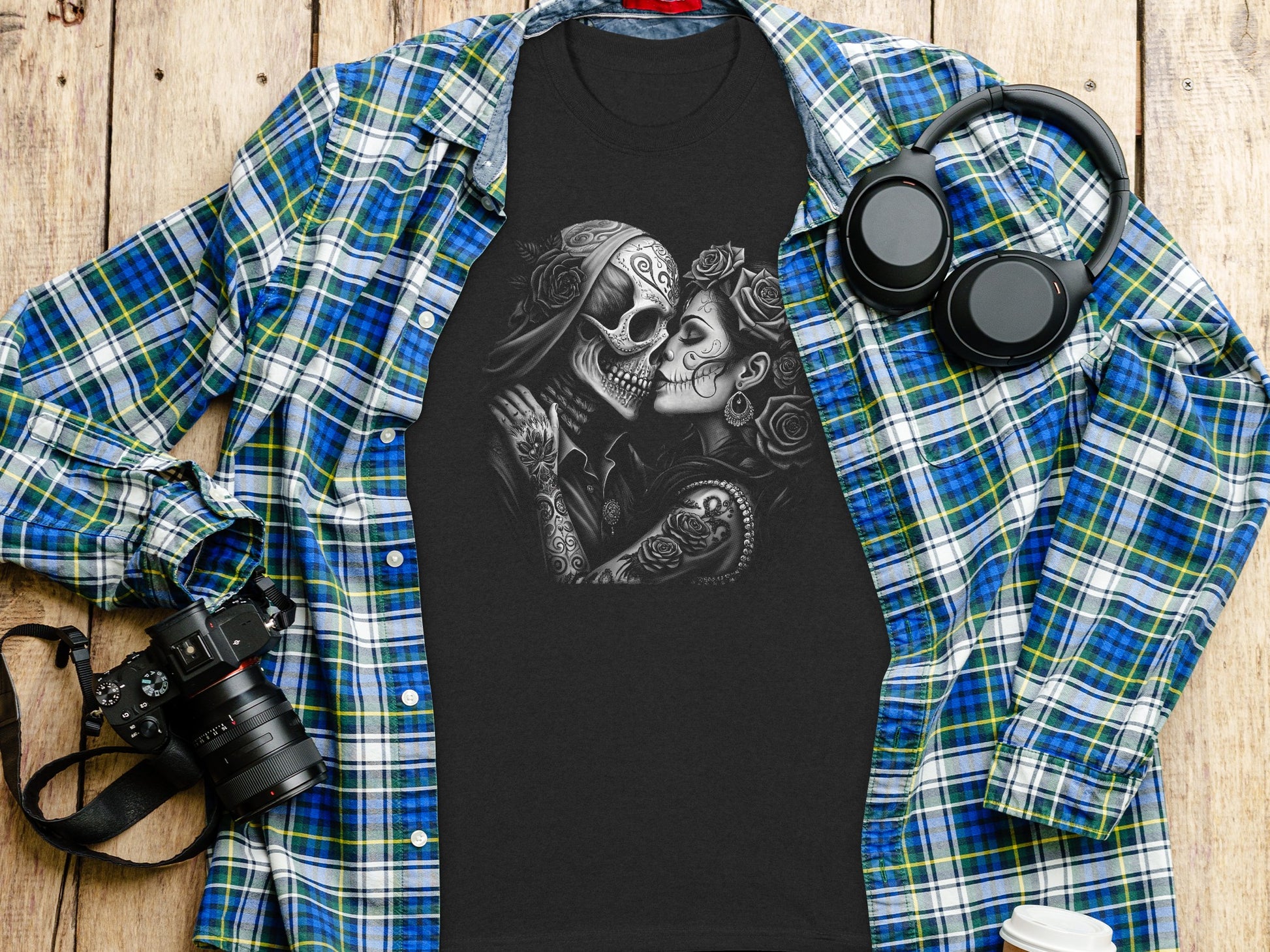 Black t-shirt with skull couple graphic, laid on a plaid shirt with headphones.