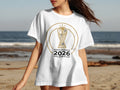 White t-shirt with 2026 FIFA World Cup trophy logo on beach background.