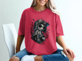 Woman wearing a red t-shirt with a skull graphic, jeans, sitting on a chair.